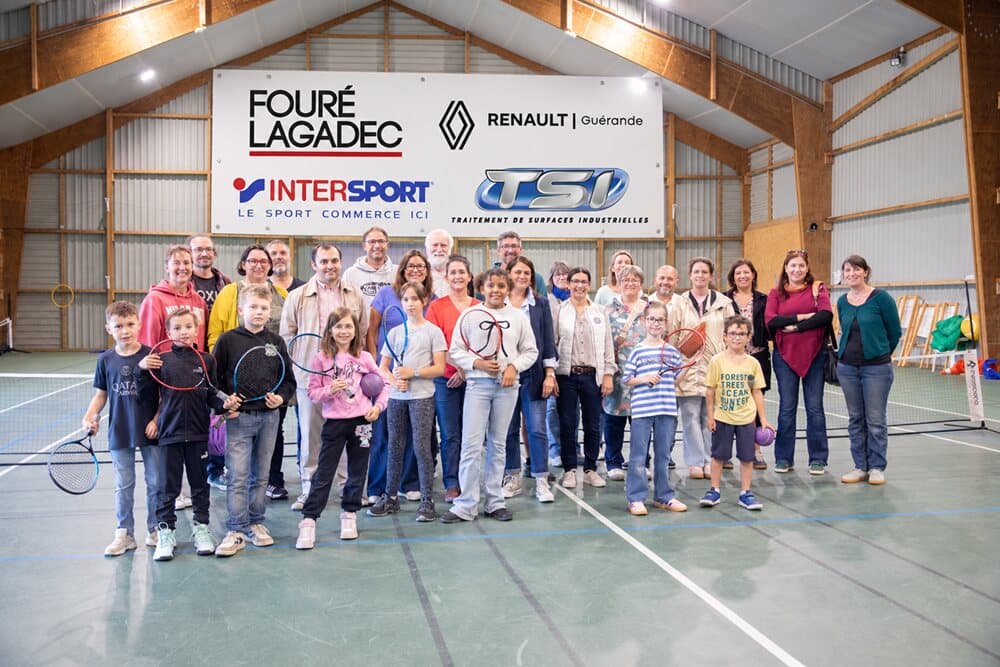Enfants, partenaires et membres du club réunis dans la salle de tennis devant la banderole des partenaires